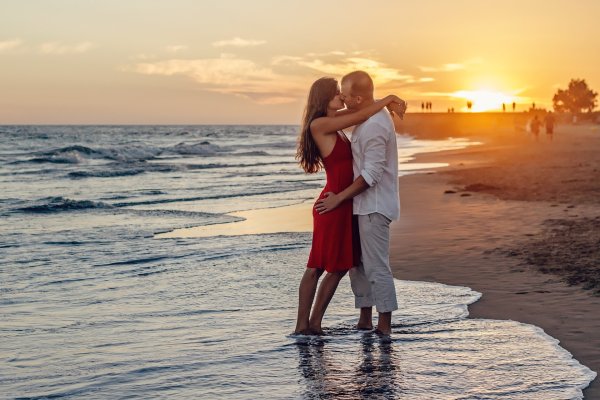 couple kissing on a beach with feet in the ocean